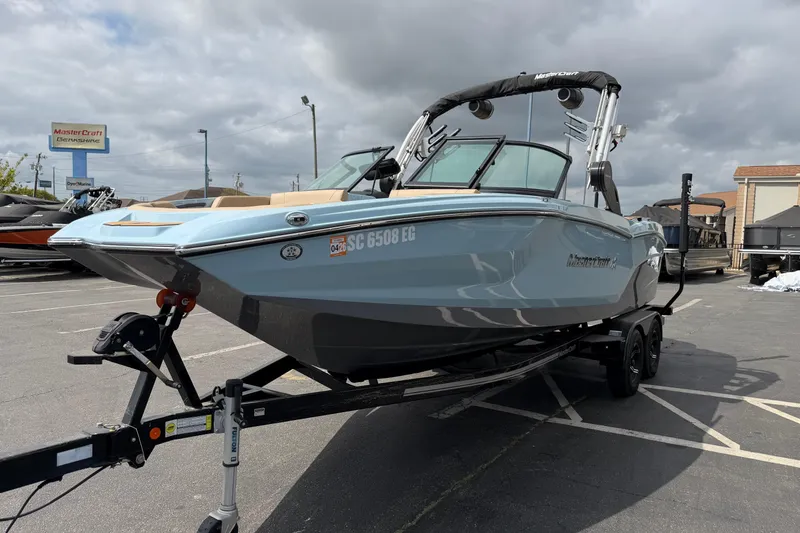 The Image of 2025 MasterCraft NXT22 boat on trailer in parking lot under cloudy sky. - 1