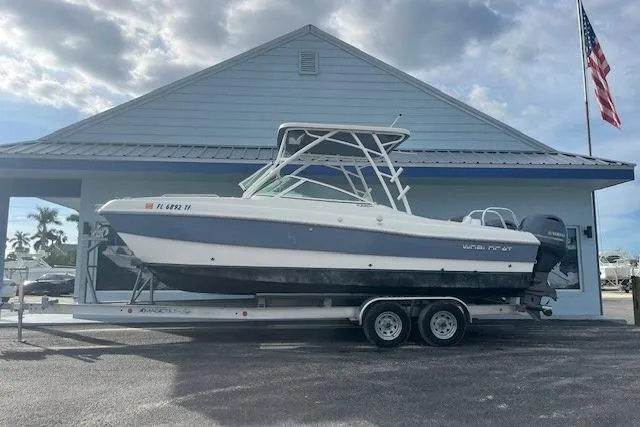 The Image of 2022 World Cat 230 SD boat on trailer, parked outside a building with an American flag. - 1