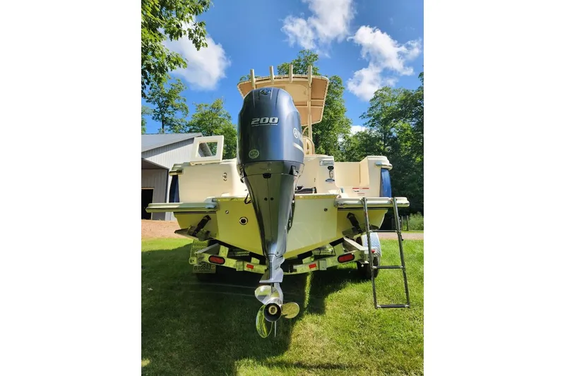 Slide: The Image of 2022 Scout 215 XSF boat with powerful outboard motor, parked on grass under blue sky. - 2