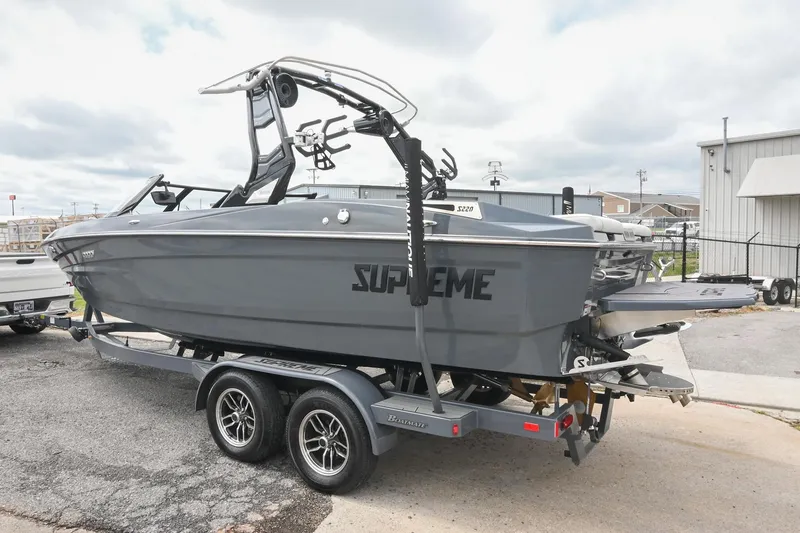 Slide: The Image of 2024 Supreme S220 boat on trailer, gray exterior, parked outdoors. - 14
