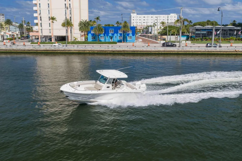 Slide: The Image of 2021 Boston Whaler 330 Outrage cruising on a sunny waterfront with cityscape background. - 13