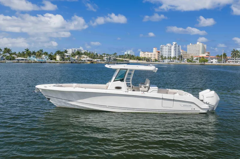Slide: The Image of 2021 Boston Whaler 330 Outrage boat on calm water with cityscape background. - 14