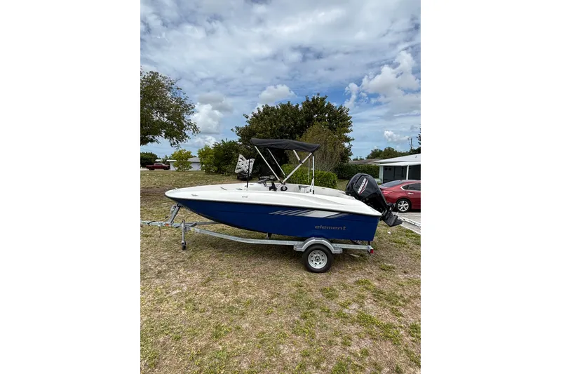 Slide: The Image of 2026 Bayliner Element E16 boat on trailer, parked outdoors under cloudy sky. - 11