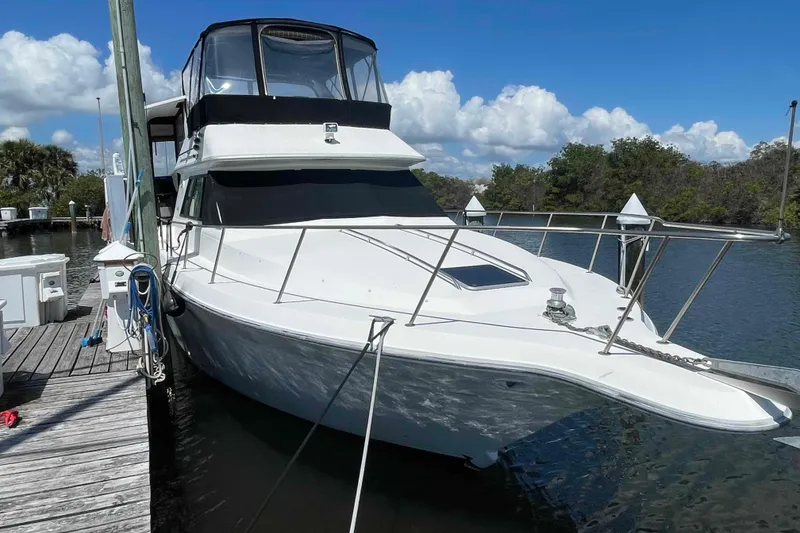The Image of 1989 Sea Ray 380 Aft Cabin yacht docked by a wooden pier under a clear sky. - 0