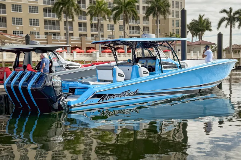 Slide: The Image of 2025 Nor-Tech 390 Sport Center Console boat docked, featuring sleek blue design and powerful engines. - 2