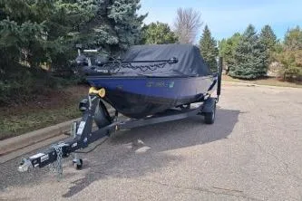 Slide: The Image of 2019 Crestliner 1850 Fish Hawk WT boat on trailer, covered, parked on a tree-lined street. - 3