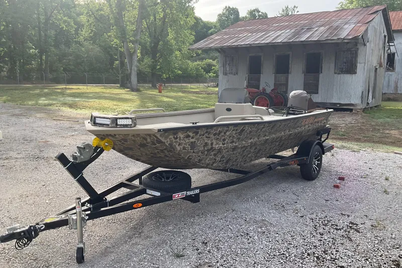 The Image of 2026 Excel 1751 River Warrior SC boat on trailer, parked outdoors near rustic building. - 0