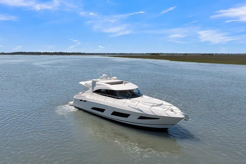 Slide: The Image of 2020 Riviera 4800 Sport Yacht cruising on a calm, scenic waterway under a clear blue sky. - 6