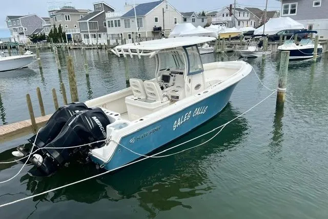 The Image of 2014 Sailfish 270 CC boat docked in a marina, featuring twin outboard engines. - 0