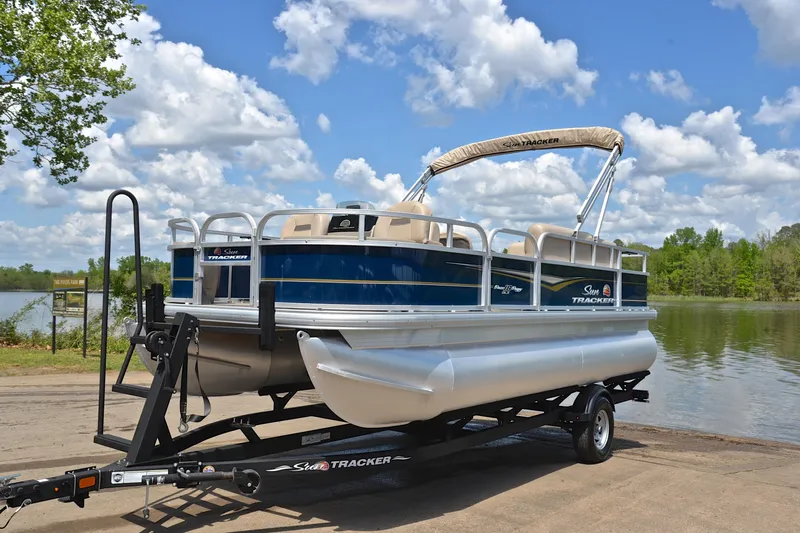 Slide: The Image of 2024 Sun Tracker Bass Buggy 18 DLX pontoon boat on trailer by a lake. - 10