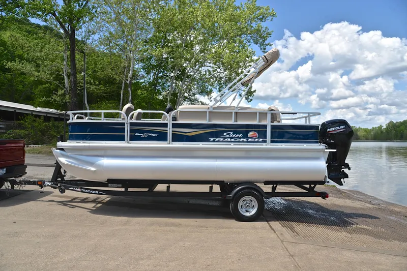Slide: The Image of 2024 Sun Tracker Bass Buggy 18 DLX pontoon boat on trailer by a lake. - 11
