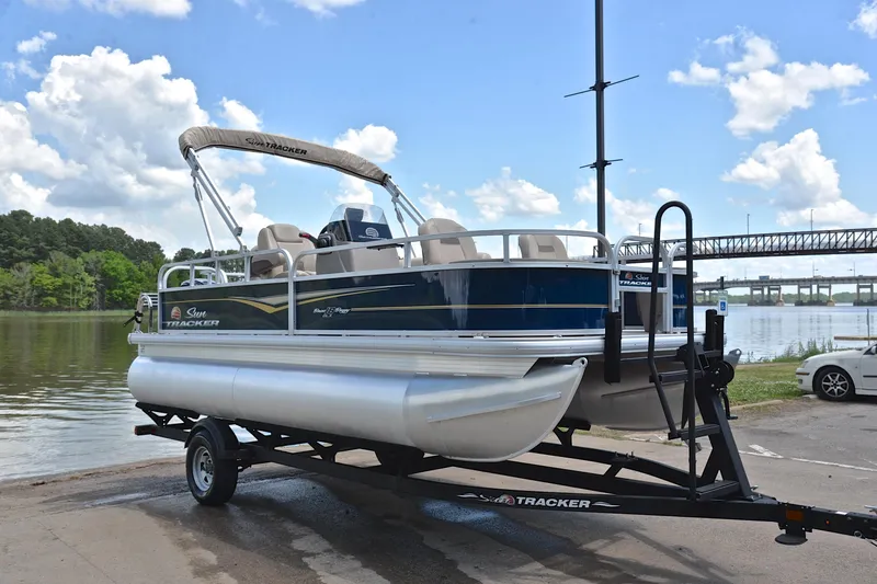 Slide: The Image of 2024 Sun Tracker Bass Buggy 18 DLX pontoon boat on trailer by a scenic lake. - 16