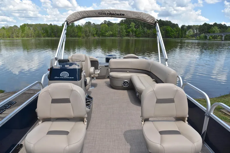 Slide: The Image of 2024 Sun Tracker Bass Buggy 18 DLX pontoon boat on a serene lake with plush seating. - 20
