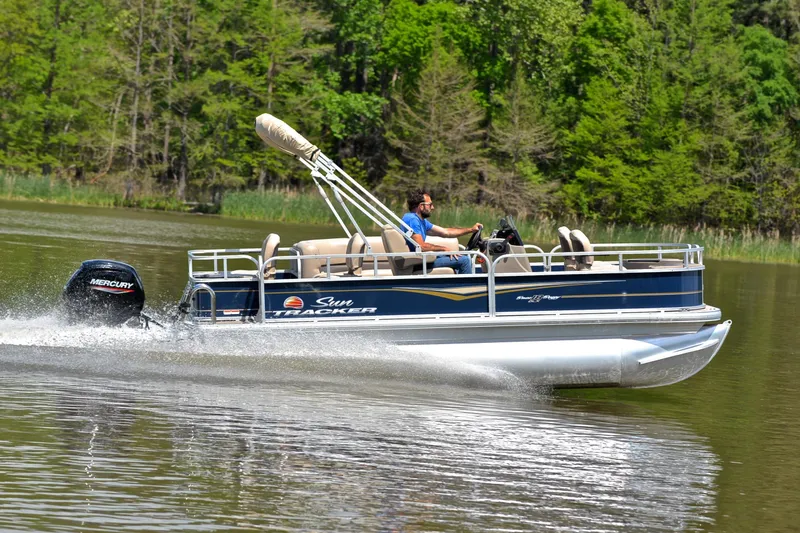 Slide: The Image of 2024 Sun Tracker Bass Buggy 18 DLX pontoon boat cruising on a lake. - 3