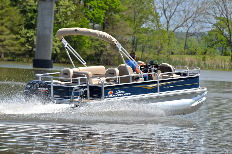Slide: The Image of 2024 Sun Tracker Bass Buggy 18 DLX pontoon boat cruising on a serene lake. - 5