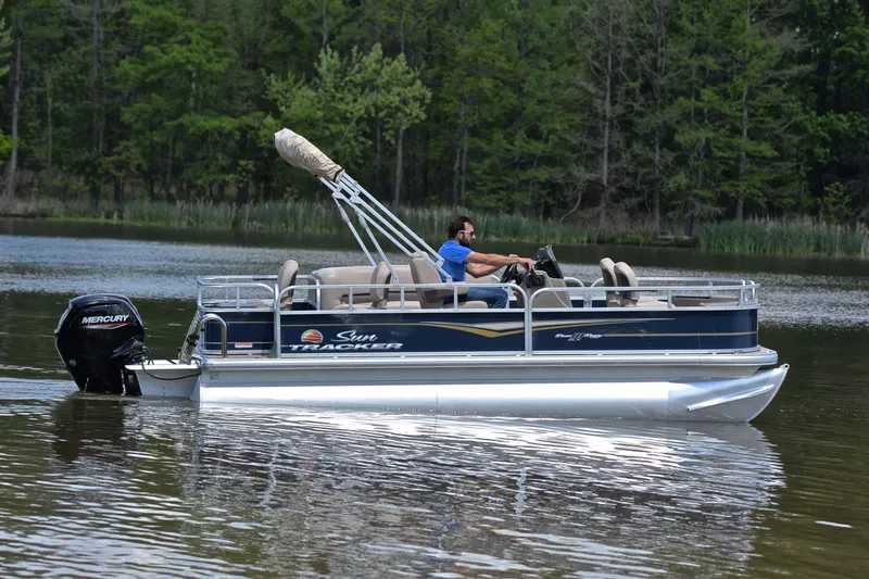 Slide: The Image of 2024 Sun Tracker Bass Buggy 18 DLX pontoon boat cruising on a serene lake. - 6