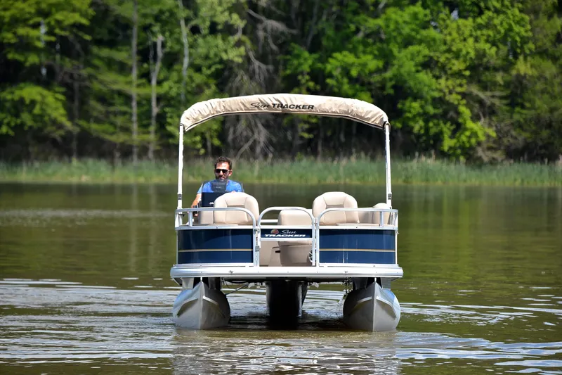 Slide: The Image of 2024 Sun Tracker Bass Buggy 18 DLX pontoon boat cruising on a serene lake. - 9