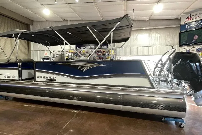 Slide: The Image of 2024 Premier 270 Intrigue pontoon boat displayed indoors with canopy and Mercury engine. - 2