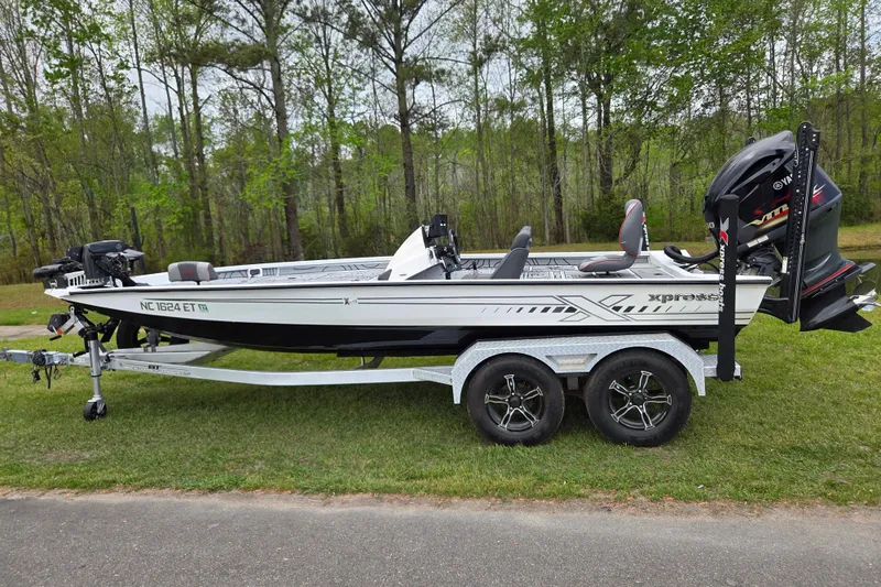 The Image of 2021 Xpress X21 Pro boat on trailer, parked on grass with forest background. - 0