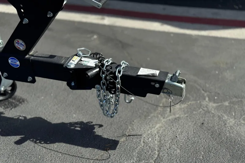Slide: The Image of Trailer hitch of 2024 Yamaha Boats 252XE with safety chains on asphalt. - 45