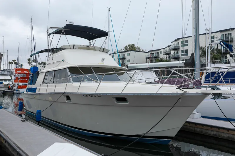 The Image of 1991 Silverton 41 Aft Cabin yacht docked at marina, overcast sky, modern buildings in background. - 0