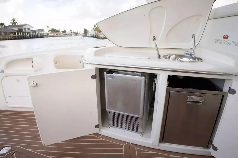 Slide: The Image of 1999 Cranchi Mediterranee 41 yacht kitchenette with sink, fridge, and storage, docked by waterfront homes. - 10