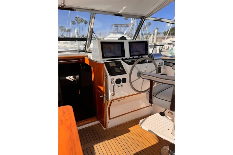 Slide: The Image of 1999 Grand Banks 38 Eastbay EX helm with dual screens and wooden accents in a marina setting. - 14