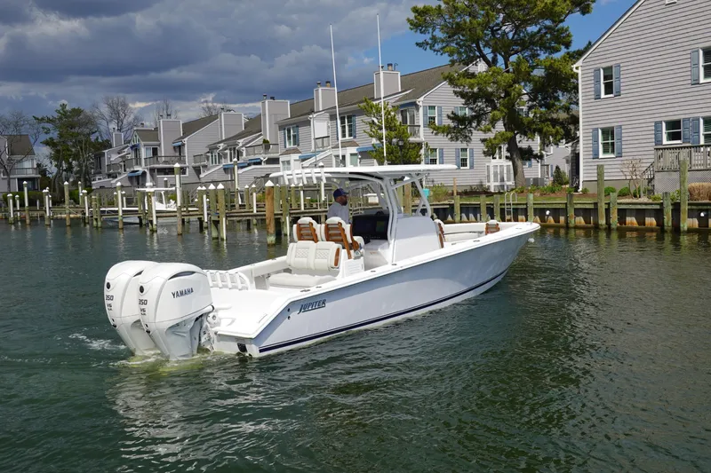 The Image of 2026 Jupiter 32 FS boat cruising near waterfront homes under cloudy skies. - 1