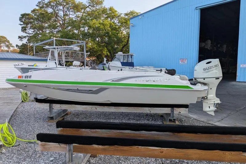 The Image of 2018 Starcraft MDX 211 O/B boat with Suzuki outboard motor, docked near blue building. - 1