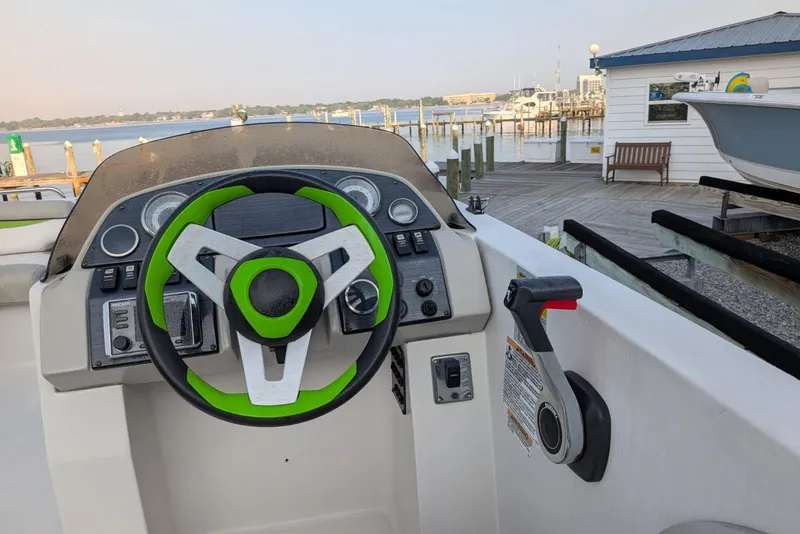 Slide: The Image of 2018 Starcraft MDX 211 O/B boat dashboard with green-accented steering wheel at marina. - 6