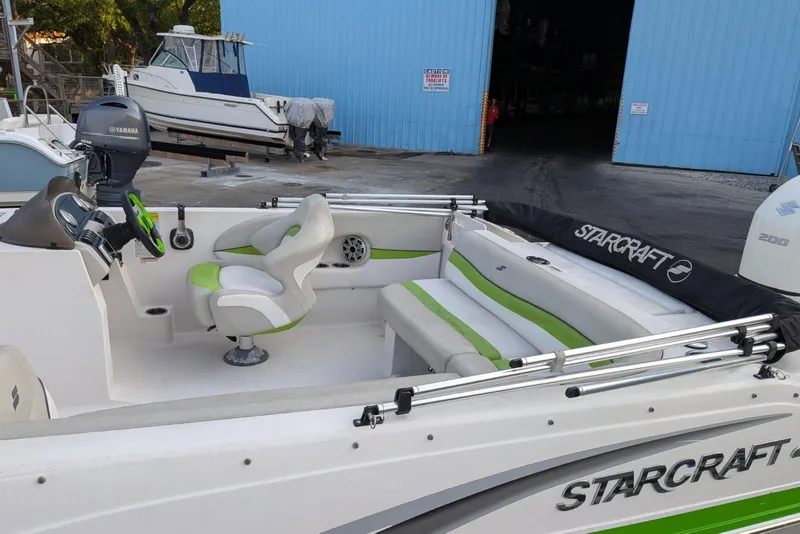 Slide: The Image of 2018 Starcraft MDX 211 O/B boat with green and white interior, docked near blue warehouse. - 7