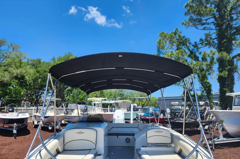 Slide: The Image of 2024 Stingray 212 SC boat with canopy, parked outdoors under a clear blue sky. - 11