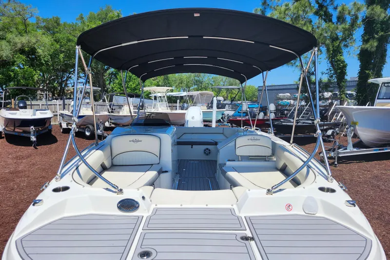 Slide: The Image of 2024 Stingray 212 SC boat with canopy, docked outdoors under clear blue sky. - 12