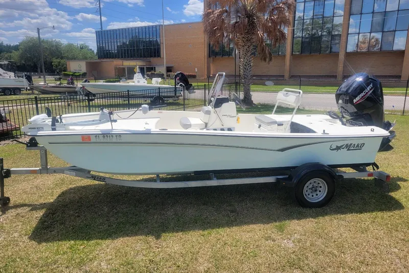 The Image of 2024 Mako Pro Skiff 17 CC boat on trailer, parked on grass, with a Mercury outboard motor. - 1