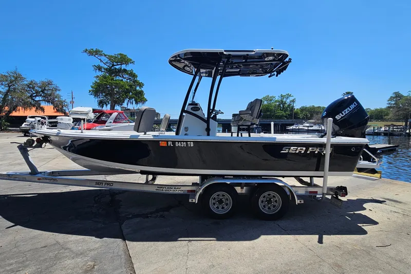 Slide: The Image of 2022 Sea Pro 228 Bay boat on trailer, parked near waterfront under clear blue sky. - 7