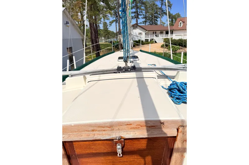 Slide: The Image of 1984 Island Packet sailboat deck with ropes and wooden hatch, surrounded by trees and buildings. - 15