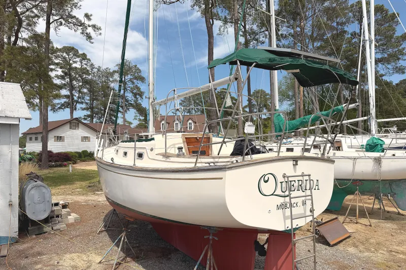 Slide: The Image of 1984 Island Packet sailboat "Querida" on land, surrounded by trees and buildings. - 3