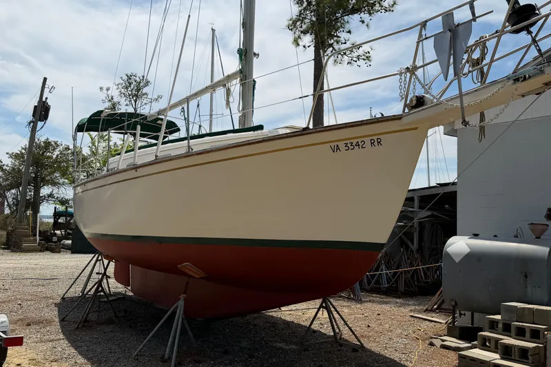 Slide: The Image of 1984 Island Packet sailboat on stands, hull painted red and white, outdoors. - 42