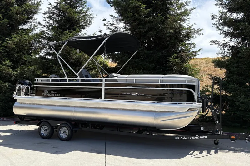 Slide: The Image of 2026 Sun Tracker SportFish 22 DLX pontoon boat on trailer, parked outdoors. - 2