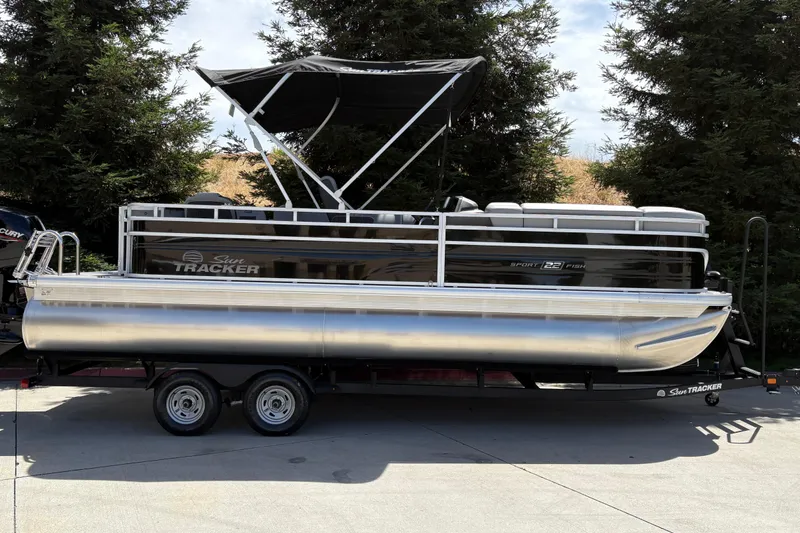 The Image of 2026 Sun Tracker SportFish 22 DLX pontoon boat on trailer, parked outdoors. - 0