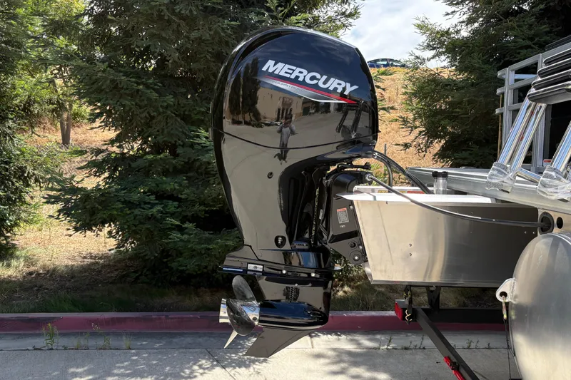 Slide: The Image of 2026 Sun Tracker SportFish 22 DLX with Mercury outboard motor, parked near trees. - 9