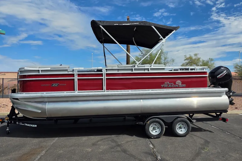 Slide: The Image of 2026 Sun Tracker SportFish 22 DLX pontoon boat on trailer, under clear blue sky. - 1