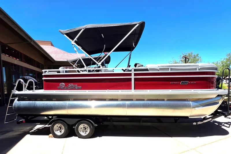 Slide: The Image of 2026 Sun Tracker SportFish 22 DLX pontoon boat with canopy on trailer, side view. - 2
