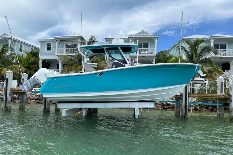 The Image of 2021 Blackfin 272 CC boat docked near waterfront homes, turquoise hull visible. - 1