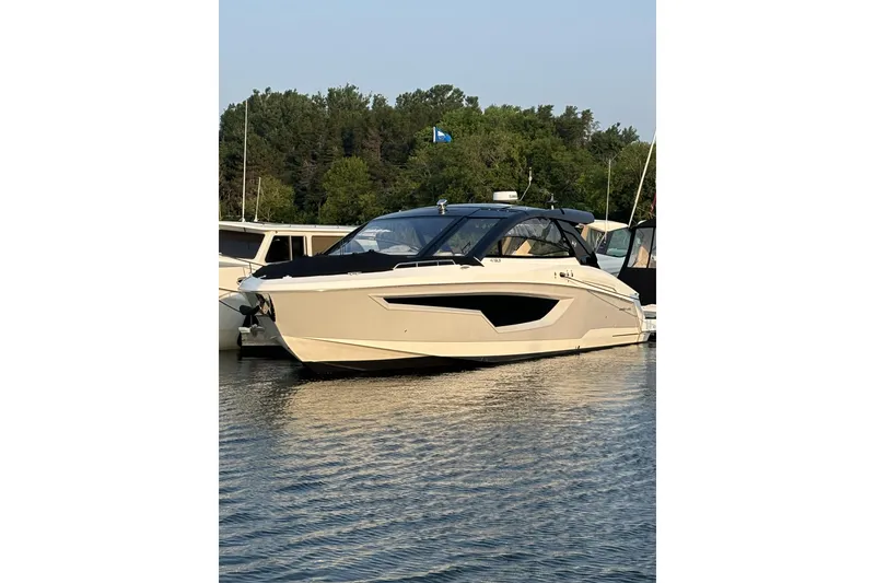 Slide: The Image of 2024 Cruisers Yachts 42 GLS OB in water, docked near lush greenery. - 2