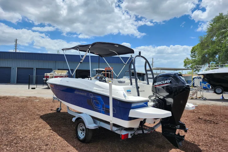 Slide: The Image of 2021 Bayliner Element E18 boat with Mercury engine, parked outdoors under a blue sky. - 5