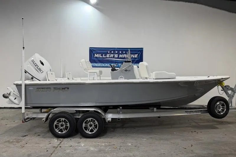 The Image of 2026 Sea Pro 210 Bay boat on trailer in showroom, featuring Suzuki engine. - 0