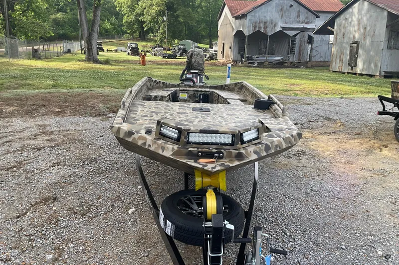 Slide: The Image of Camouflage-patterned 2026 Excel 1751 Viper F4 boat on trailer, rustic background. - 3