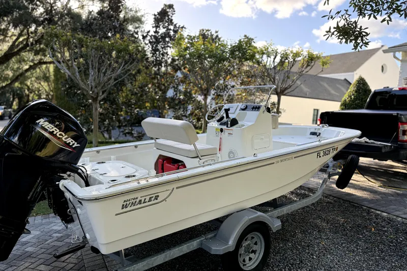 The Image of 2023 Boston Whaler 150 Montauk boat on trailer, parked outdoors under cloudy sky. - 1