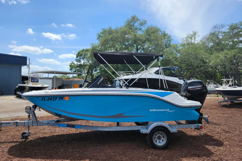 Slide: The Image of 2023 Bayliner Element M17 boat on trailer, blue hull, parked outdoors. - 4